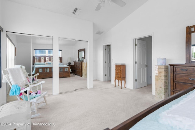 carpeted bedroom with ceiling fan, multiple closets, and high vaulted ceiling