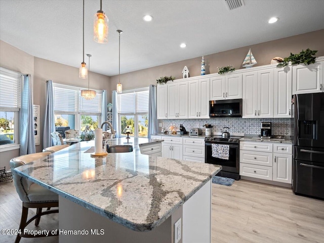 kitchen with white cabinetry, sink, black appliances, a spacious island, and light hardwood / wood-style flooring