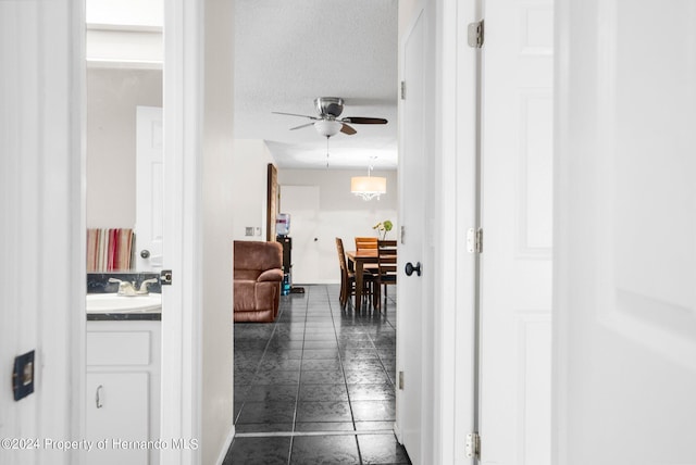 hallway with dark tile patterned floors, sink, and a textured ceiling