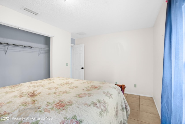 bedroom featuring a textured ceiling, light tile patterned floors, and a closet