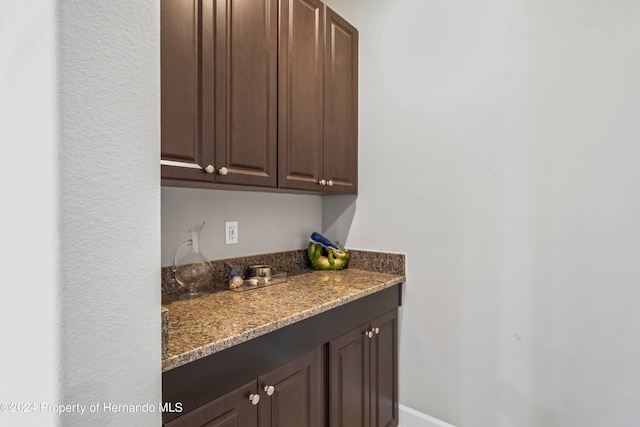 bar with dark brown cabinets and dark stone counters