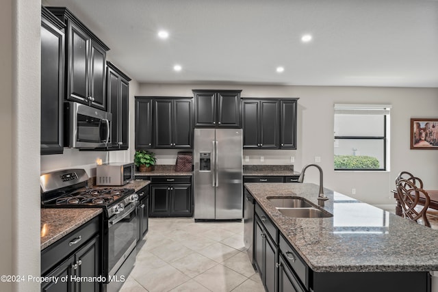 kitchen with appliances with stainless steel finishes, dark stone counters, sink, an island with sink, and light tile patterned flooring