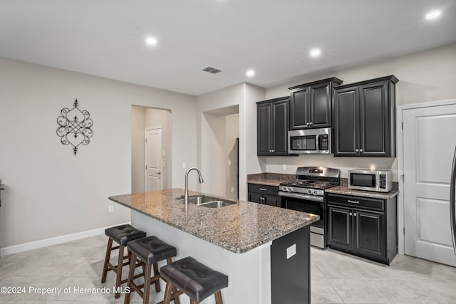 kitchen with a kitchen breakfast bar, stainless steel appliances, a kitchen island with sink, sink, and stone counters