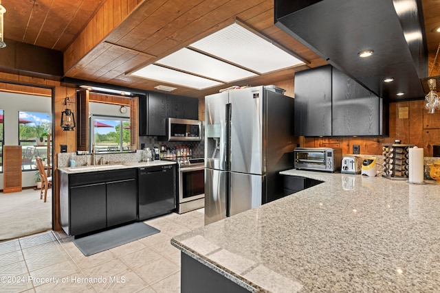 kitchen featuring stainless steel appliances, wood walls, light tile patterned flooring, and light stone countertops