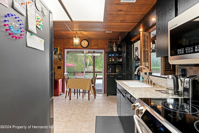 kitchen with wood walls, sink, appliances with stainless steel finishes, a skylight, and wood ceiling