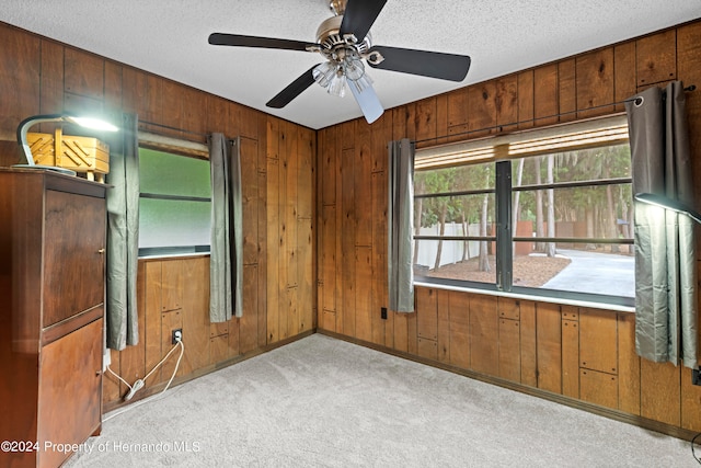 carpeted empty room with ceiling fan, wooden walls, and a textured ceiling