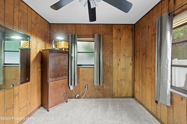 interior space with light colored carpet, wooden walls, and ceiling fan