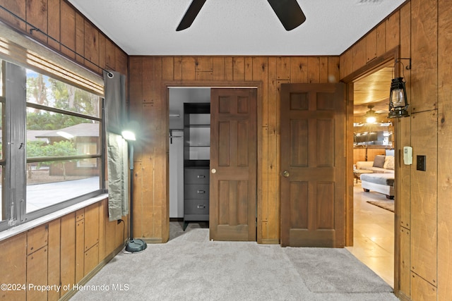 carpeted bedroom with wooden walls, a textured ceiling, and ceiling fan