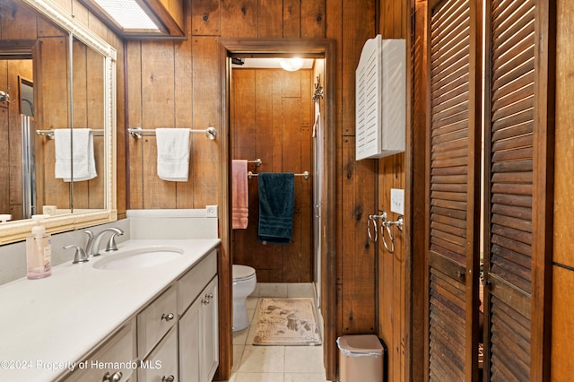 bathroom with toilet, vanity, wooden walls, and tile patterned floors