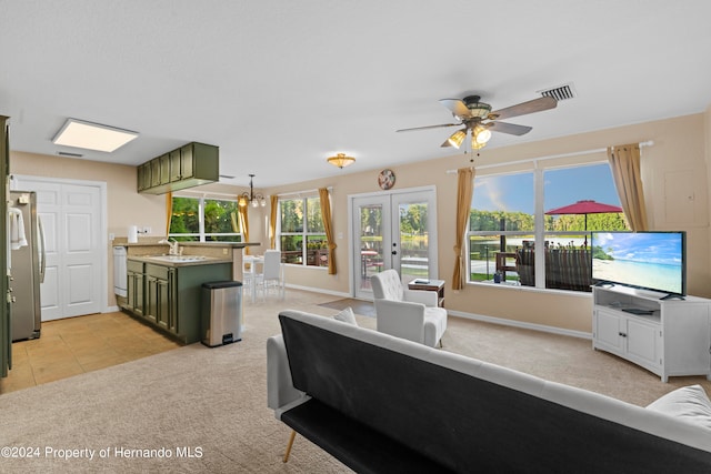 carpeted living room featuring ceiling fan with notable chandelier, sink, and french doors