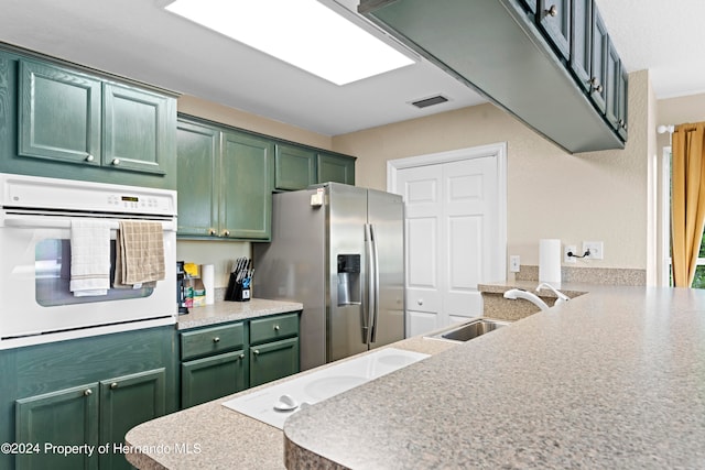 kitchen with kitchen peninsula, sink, green cabinetry, and white oven