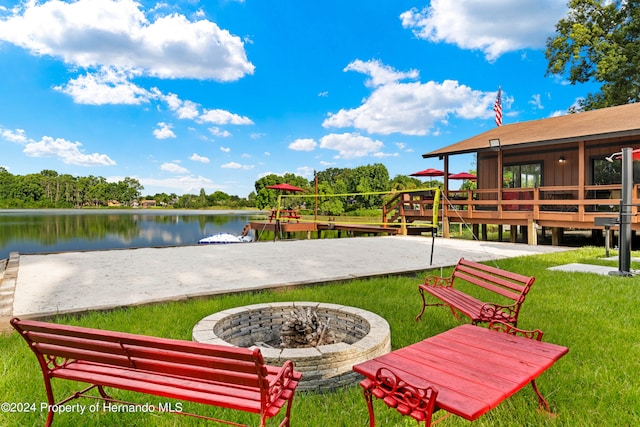 view of community featuring a deck with water view, a lawn, and a fire pit