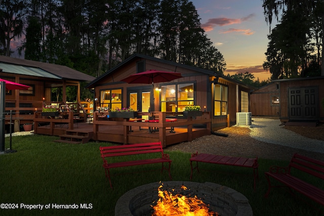 back house at dusk with central AC, a yard, a fire pit, and a wooden deck