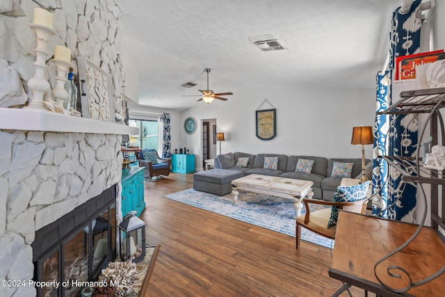 living room with ceiling fan, dark hardwood / wood-style floors, a textured ceiling, and a stone fireplace