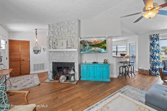 living room with lofted ceiling, a textured ceiling, hardwood / wood-style flooring, ceiling fan, and a fireplace