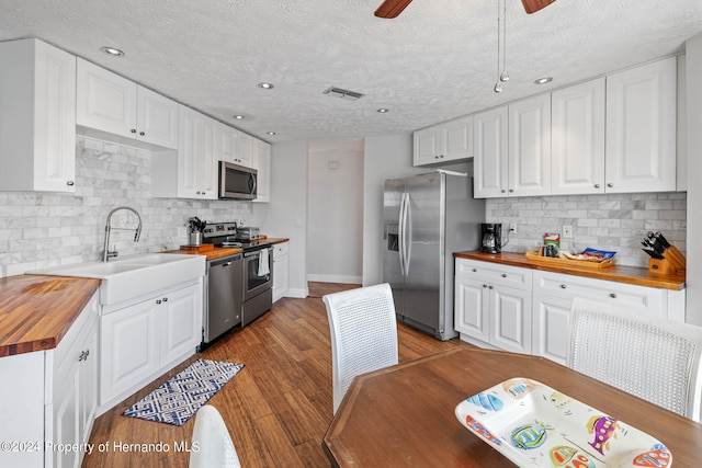 kitchen with hardwood / wood-style flooring, backsplash, wood counters, white cabinetry, and appliances with stainless steel finishes