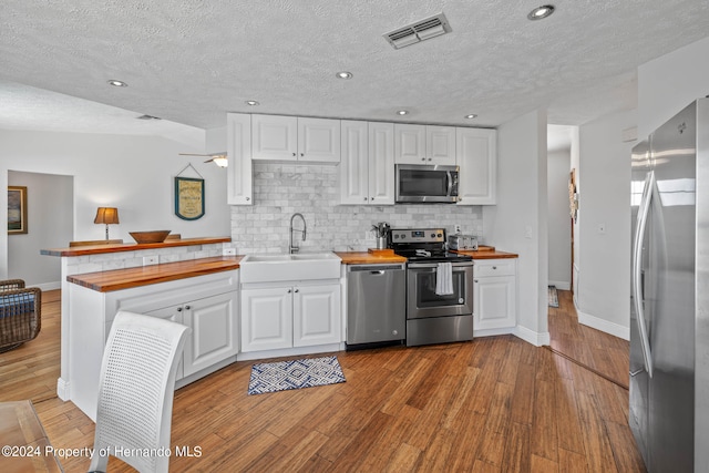 kitchen with white cabinets, appliances with stainless steel finishes, butcher block counters, and light hardwood / wood-style flooring