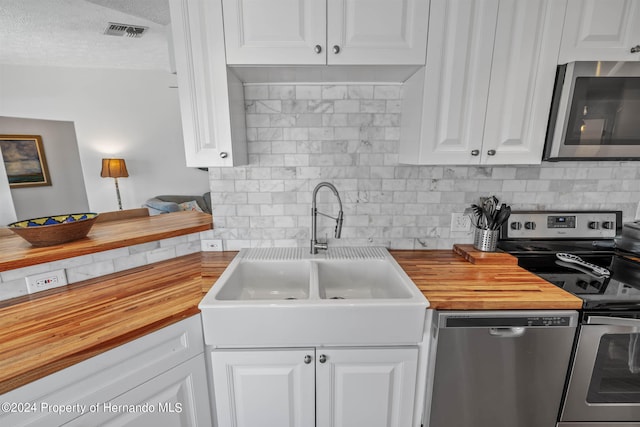 kitchen featuring wooden counters, tasteful backsplash, white cabinets, and stainless steel appliances