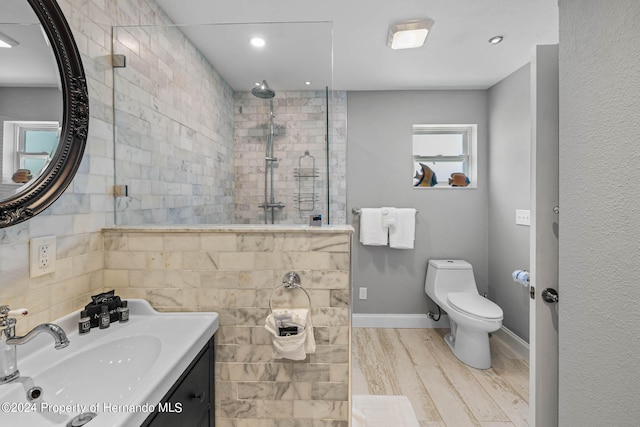 bathroom with toilet, wood-type flooring, a tile shower, and vanity