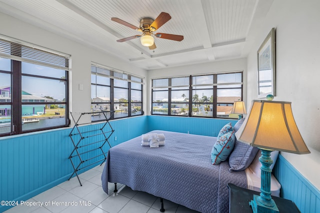 tiled bedroom featuring wood walls, beamed ceiling, multiple windows, and ceiling fan