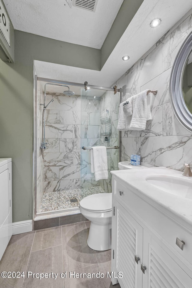 bathroom featuring a shower with door, vanity, a textured ceiling, and washer / dryer