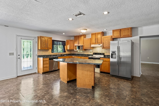 kitchen with stainless steel appliances, a textured ceiling, a breakfast bar area, a kitchen island, and backsplash