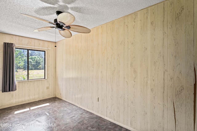 spare room with wood walls, a textured ceiling, and ceiling fan