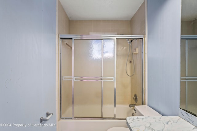 full bathroom with toilet, vanity, a textured ceiling, and enclosed tub / shower combo