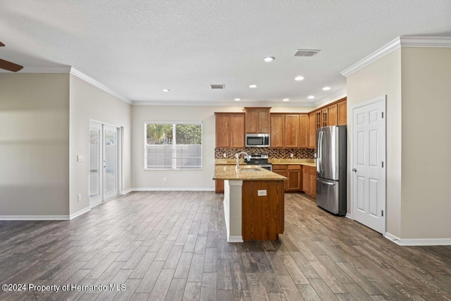 kitchen with ornamental molding, an island with sink, dark hardwood / wood-style flooring, light stone counters, and stainless steel appliances