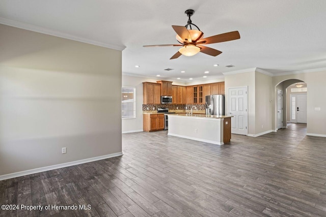 kitchen with ceiling fan, dark wood-type flooring, crown molding, a kitchen island with sink, and appliances with stainless steel finishes