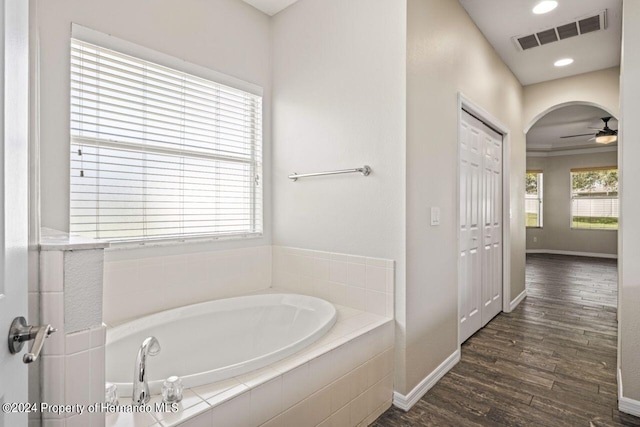 bathroom featuring ceiling fan, wood-type flooring, crown molding, and tiled tub