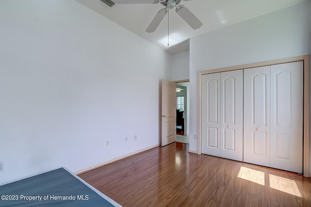 unfurnished bedroom featuring hardwood / wood-style floors, a high ceiling, ceiling fan, and a closet