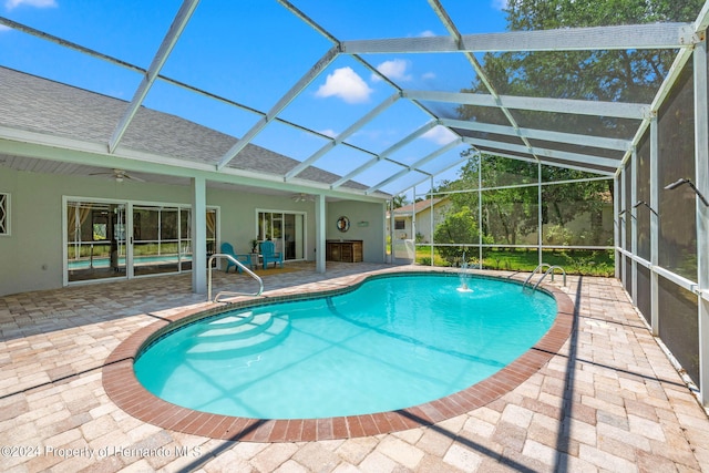 view of swimming pool with glass enclosure, ceiling fan, pool water feature, and a patio area