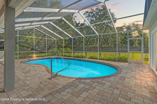 pool at dusk featuring a yard, glass enclosure, and a patio