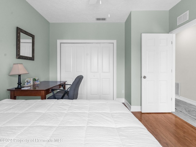 bedroom with hardwood / wood-style floors, ceiling fan, a textured ceiling, and a closet