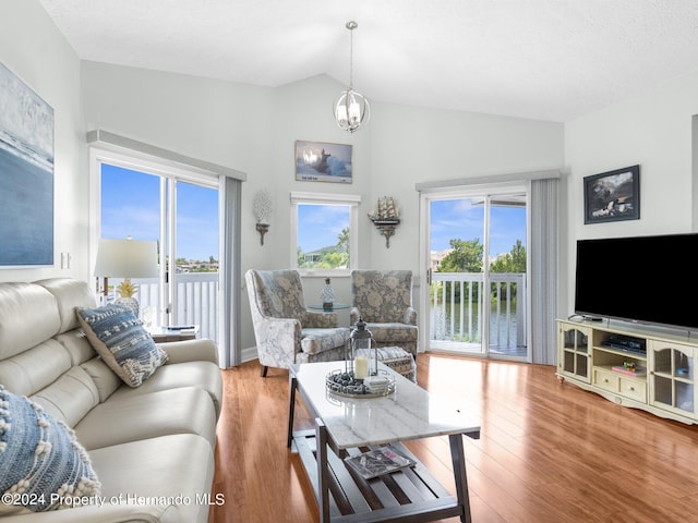 living room featuring an inviting chandelier, a healthy amount of sunlight, vaulted ceiling, and hardwood / wood-style flooring