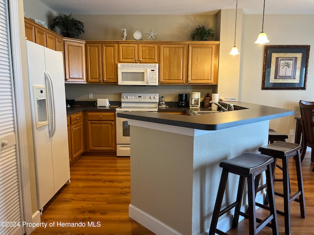 kitchen featuring dark hardwood / wood-style flooring, hanging light fixtures, sink, a breakfast bar area, and white appliances