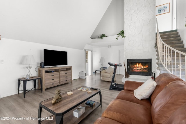 living room with a stone fireplace, high vaulted ceiling, and light hardwood / wood-style floors