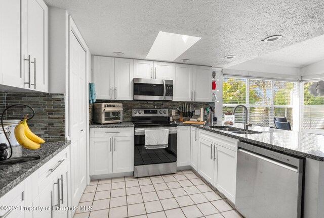 kitchen featuring sink, appliances with stainless steel finishes, a skylight, white cabinets, and decorative backsplash