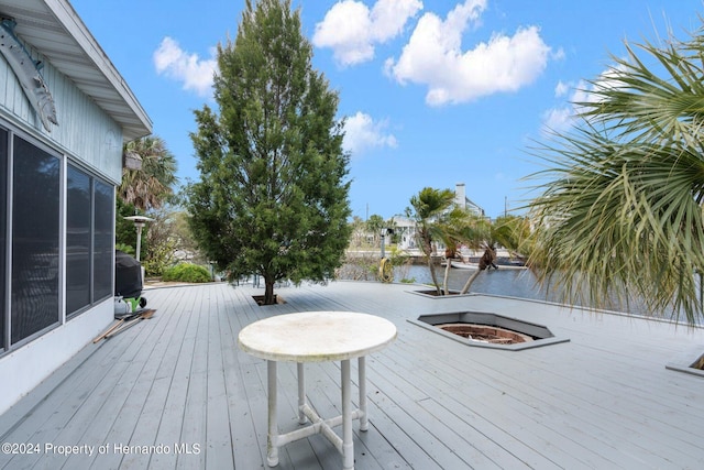 wooden deck with a sunroom, a water view, and a grill