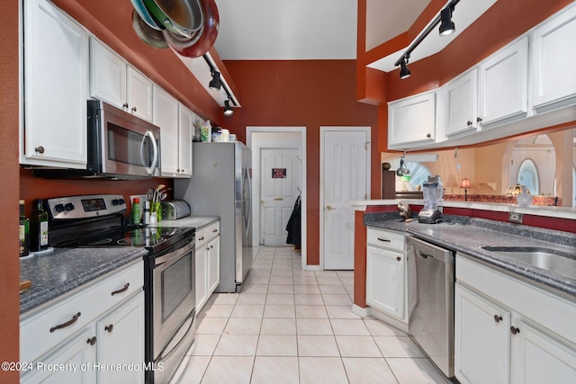 kitchen with stainless steel appliances, light tile patterned flooring, dark stone countertops, and white cabinetry