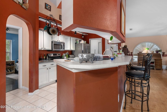 kitchen featuring stainless steel appliances, a breakfast bar, white cabinetry, and light wood-type flooring