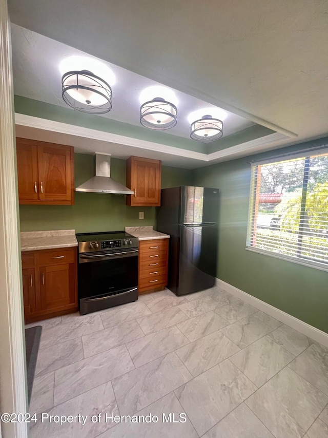 kitchen featuring stainless steel appliances, wall chimney range hood, and a tray ceiling