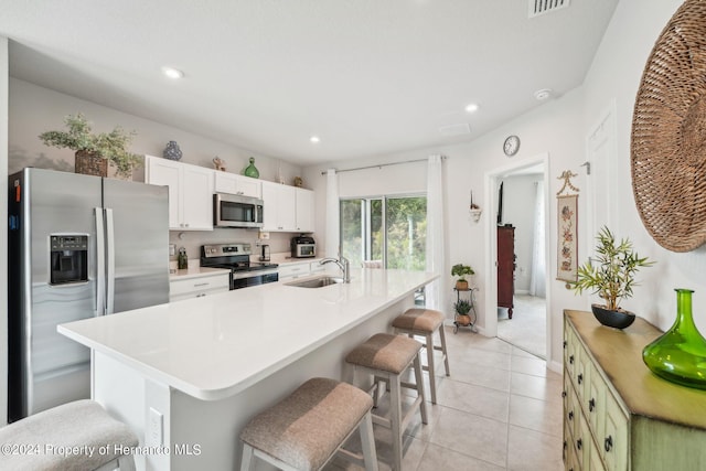 kitchen with stainless steel appliances, white cabinetry, sink, an island with sink, and a breakfast bar