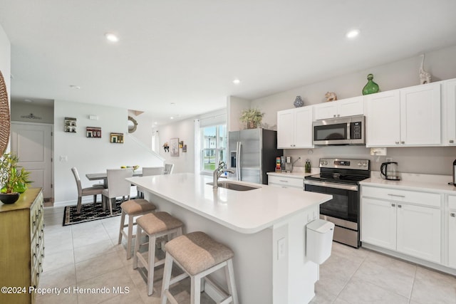 kitchen with stainless steel appliances, a breakfast bar area, white cabinetry, and an island with sink