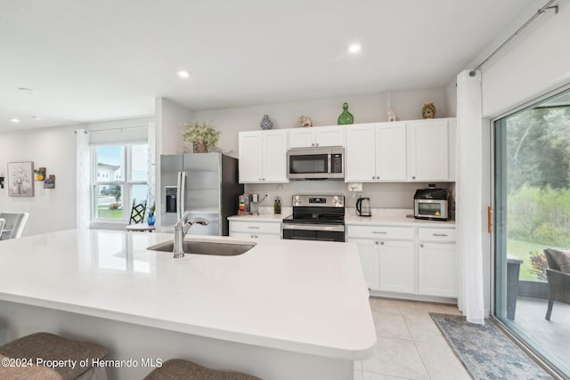 kitchen featuring white cabinets, sink, an island with sink, a kitchen breakfast bar, and appliances with stainless steel finishes