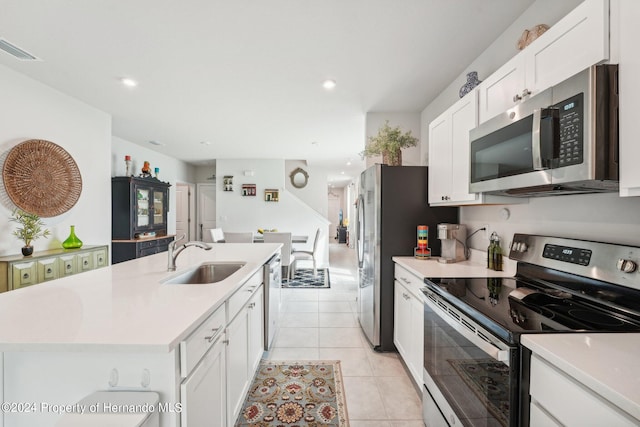 kitchen with stainless steel appliances, sink, light tile patterned floors, an island with sink, and white cabinets