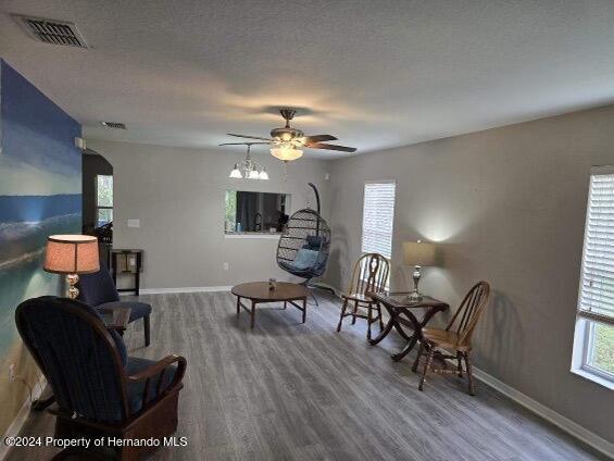 living area featuring ceiling fan, wood-type flooring, and a textured ceiling