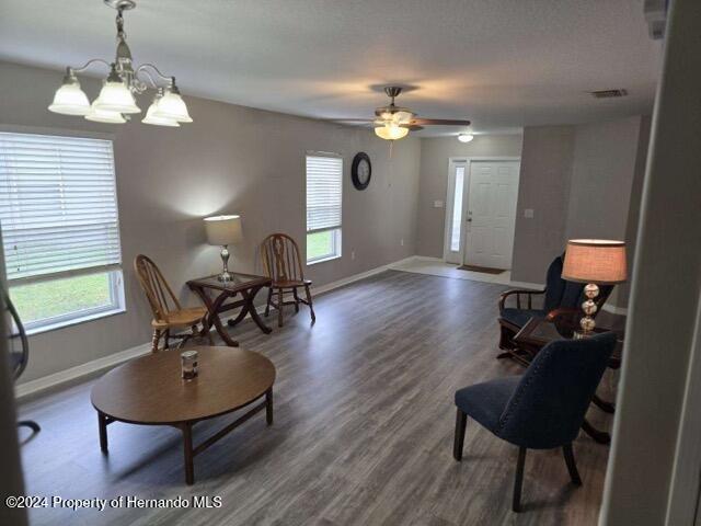 living area featuring ceiling fan with notable chandelier, wood-type flooring, and plenty of natural light