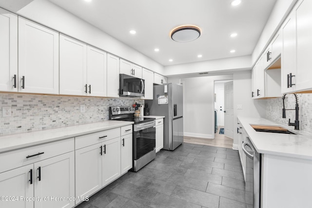 kitchen with stainless steel appliances, white cabinets, sink, tasteful backsplash, and light stone countertops